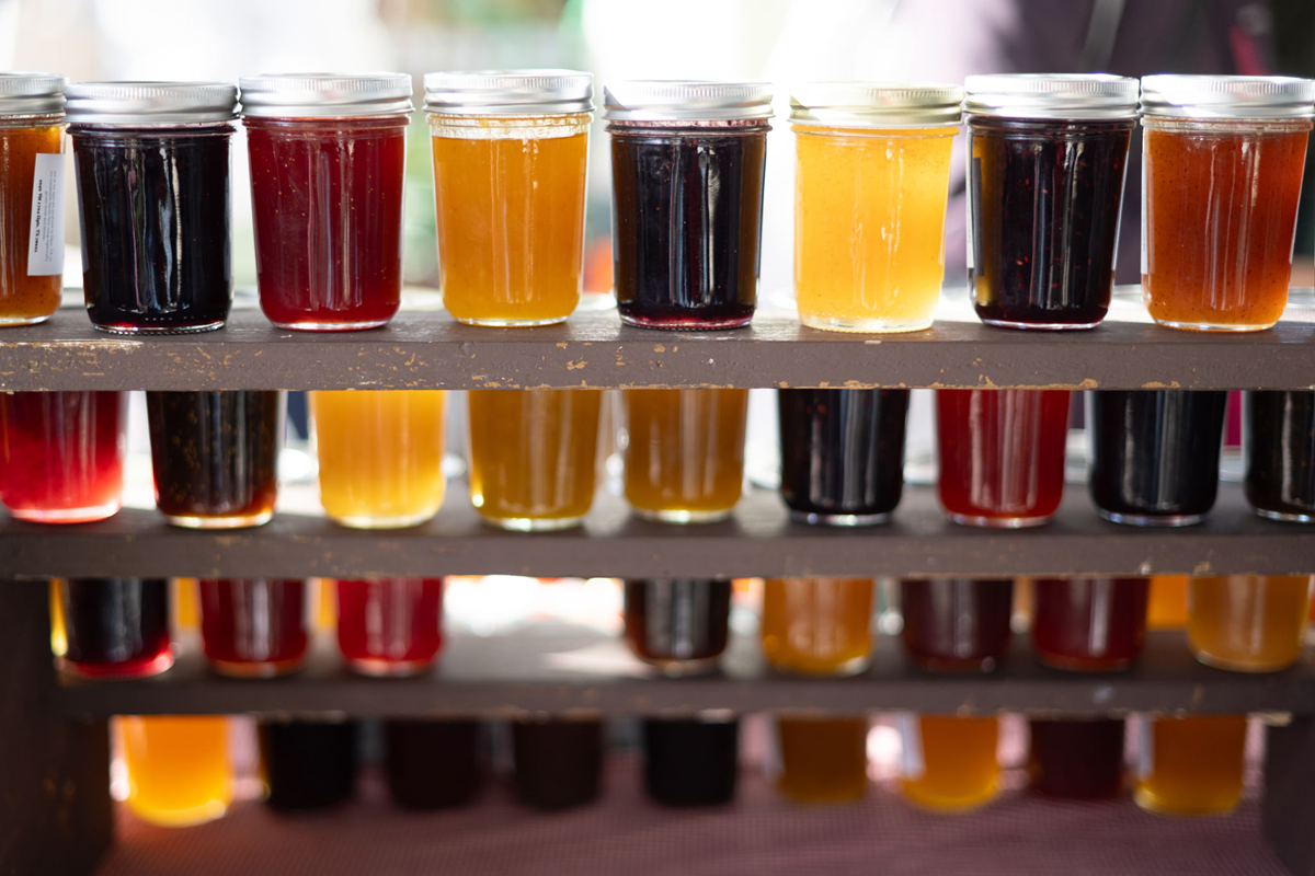 Jars of colorful honey on wooden shelves.